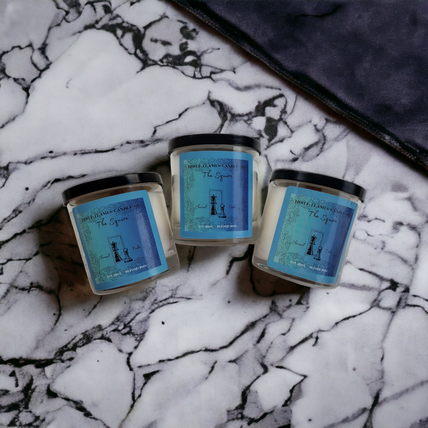 Three blue-labeled "The Squire" candles on marble background, showcasing Shopify product 10.75 OZ THE SQUIRE CANDLE with Tonka and Charcoal scent in Coconut Apricot Creme wax