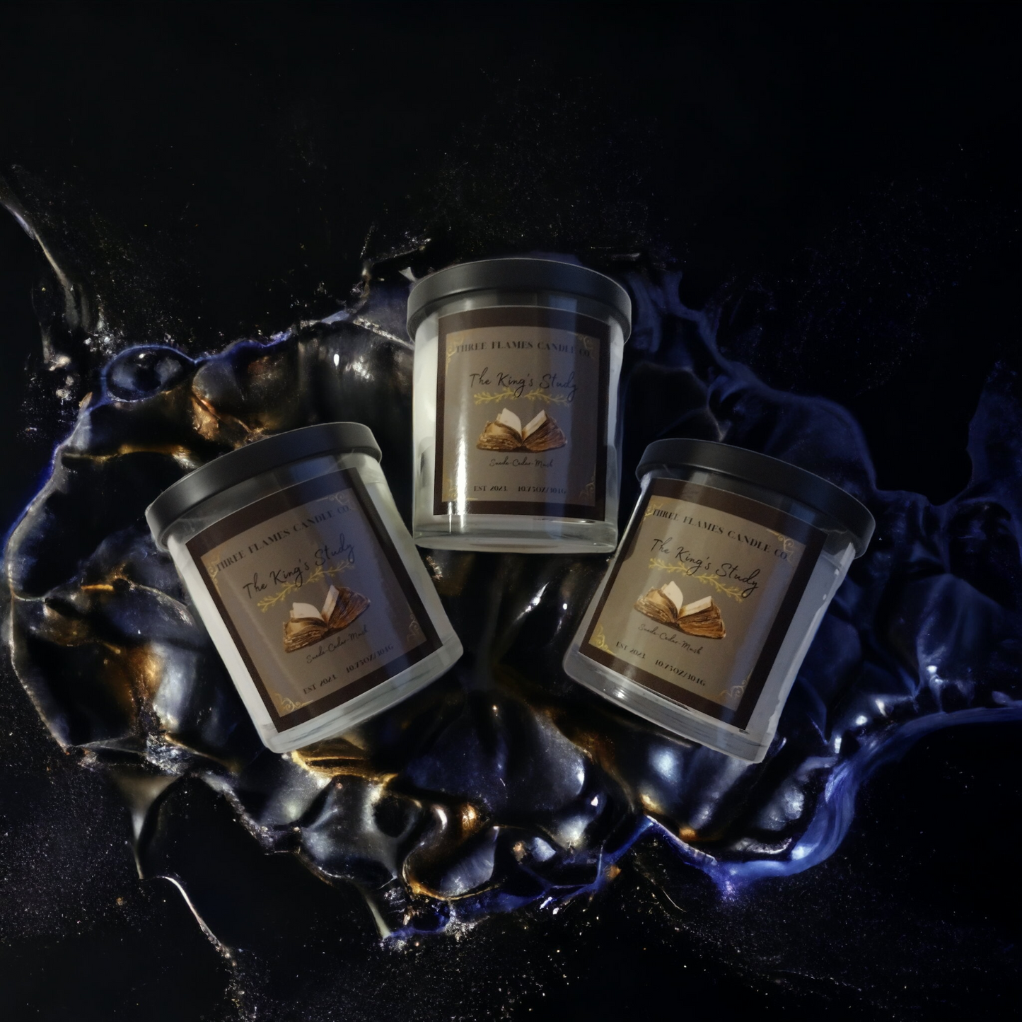 Three The King's Study candles displayed on dark background with blue and gold swirls, showcasing luxury scented candles with masculine suede, musk, and cedar fragrances in elegant glass jars