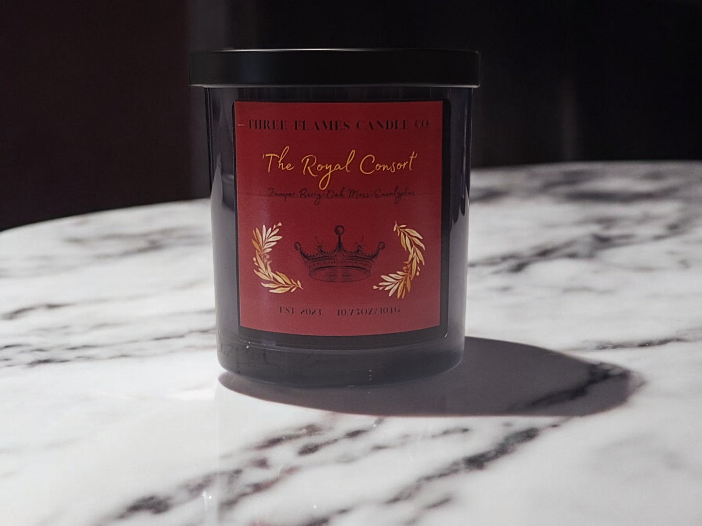 Elegant red-labeled candle "The Royal Consort" by High Flames Candle Co, featuring gold crown and laurel design, displayed on marble surface with soft shadows