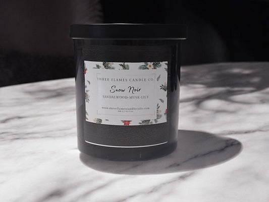 Luxurious Snow Noir candle by Three Flames Candle Co. in a black jar with white label, placed on a marble surface casting a subtle shadow, embodying winter elegance and sophistication